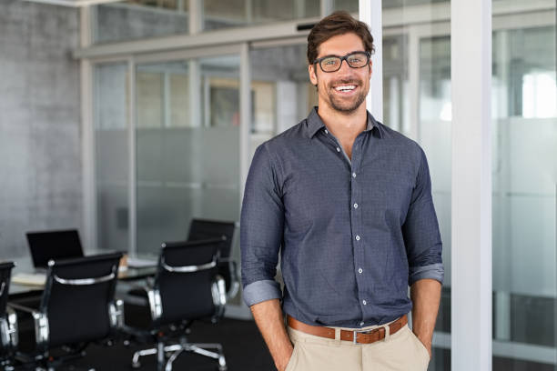 Success businessman smiling in office Portrait of young businessman wearing eyeglasses and standing outside conference room. Portrait of happy business man wearing spectacles and looking at camera with copy space. Satisfied proud man feeling confident in a modern office. dressing up photos stock pictures, royalty-free photos & images
