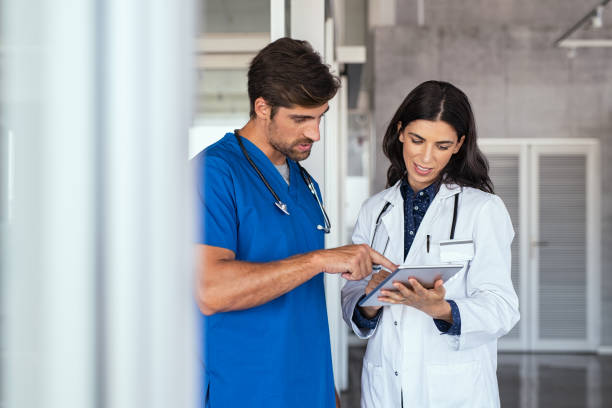 Doctor and nurse discussing report Doctor and nurse discussing over a medical report in hospital. Female mature doctor and nurse checking clinical report of patient online. Healthcare staff having discussion in a hallway of private clinic. assistant stock pictures, royalty-free photos & images