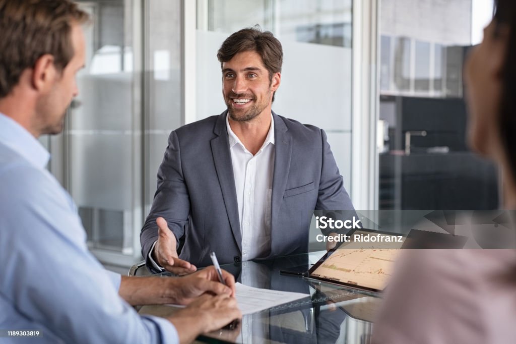 Financial advisor consulting Confident financial agent showing growth graph to couple. Mid couple meeting financial advisor for investment. Business people discussing the charts and graphs showing the results of their successful teamwork. Insurance Agent Stock Photo