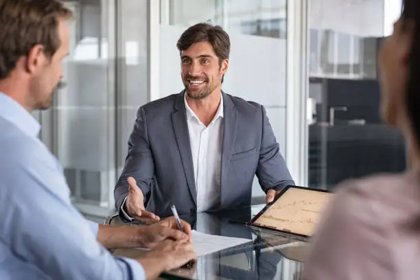 Confident financial agent showing growth graph to couple. Mid couple meeting financial advisor for investment. Business people discussing the charts and graphs showing the results of their successful teamwork.