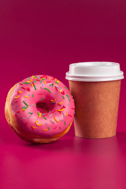 Cup of coffee and glazed round donut on a pink background