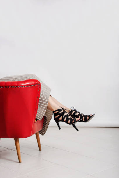 Young and trendy woman's legs with black high heeled shoes, showing up from a retro red leather armchair. Young and trendy woman's legs with black high heeled shoes, showing up from a retro red leather armchair. studio absrtact shot, bodyparts. embarrassment skirt photos stock pictures, royalty-free photos & images