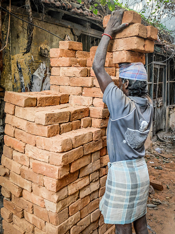 CHENNAI,TAMIL NADU/INDIA-MARCH 2nd 2018:A labourer loads a heavy weight of building bricks onto his head at a small house construction site.