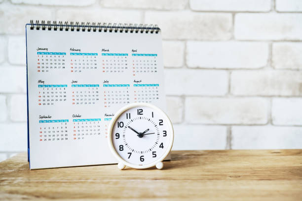 istock white analog clock with blurred calendar on wooden table 1189313549