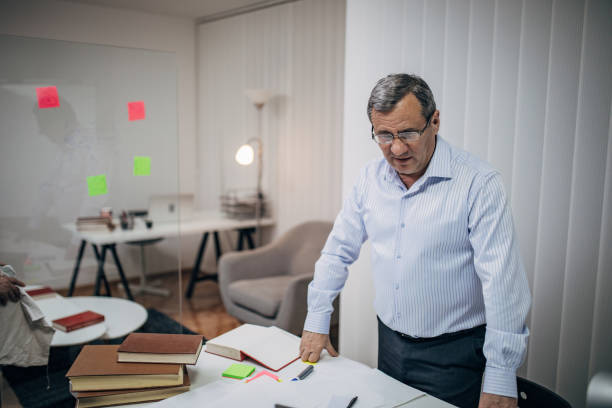 An old business man is standing at his desk An old business man is standing at his desk civil servant stock pictures, royalty-free photos & images