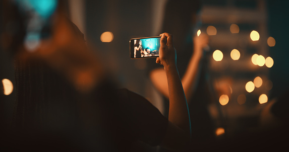 Closeup shot of an unrecognisable woman in the audience capturing a performance at the club on a cellphone