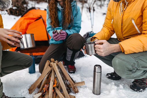 Family with coffee sitting by the campfire on snow covered landscape