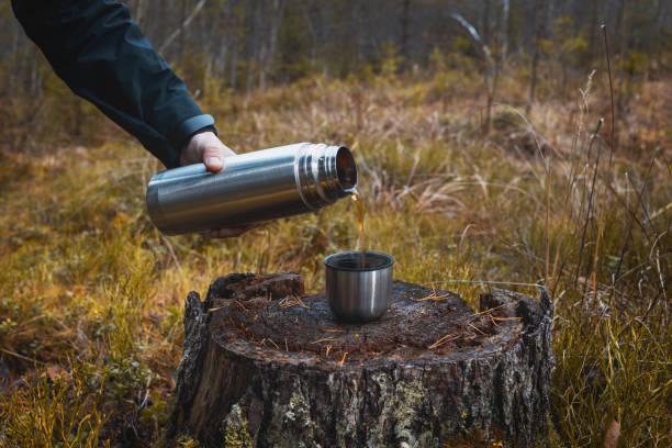 istock A man pours hot tea from a thermos into a mug on a stump. 1189321627