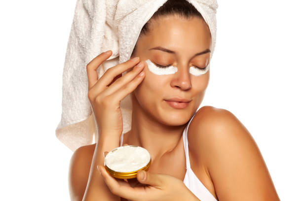 young woman applying face cream under heer eyes on white background - sensuality horizontal indoors studio shot imagens e fotografias de stock