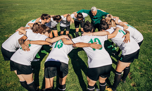 Group of women and man coach, hugging on soccer field.
