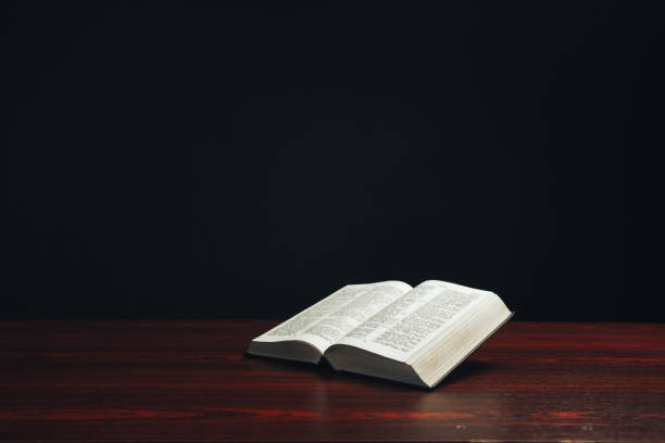 istock Open bible on a  red wooden table. Beautiful black background. 1189324469