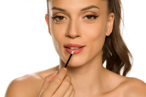 istock young beautiful woman applying lipgloss on white background 1189325311