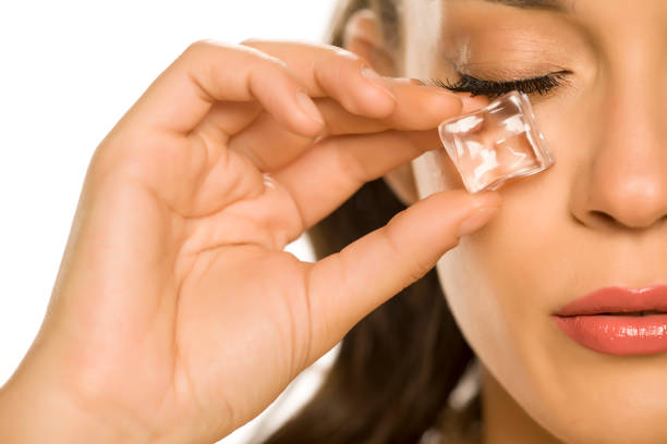 young beautiful woman holding ice cube under the eye on white background stock photo