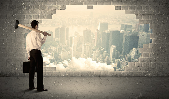 Business man hitting wall with hammer on city view background