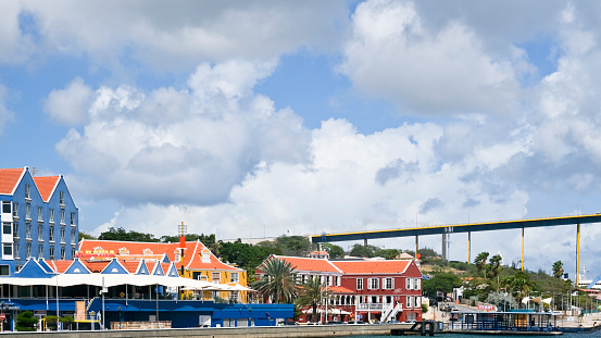 Willemstad, Curaçao - November 12, 2019: Standing on the other side of the St. Anna bay and looking at the waterfront of the historic district Otrabanda with colonial style buildings and the famous Queen Juliana bridge high up in the sky.