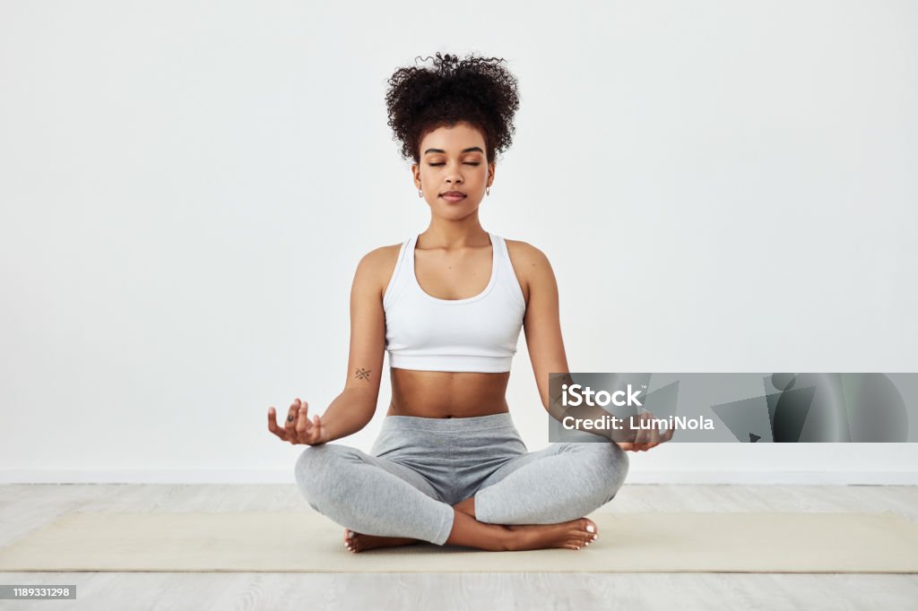 Be mindful of how awesome you are Shot of a fit young woman meditating at home Yoga Stock Photo