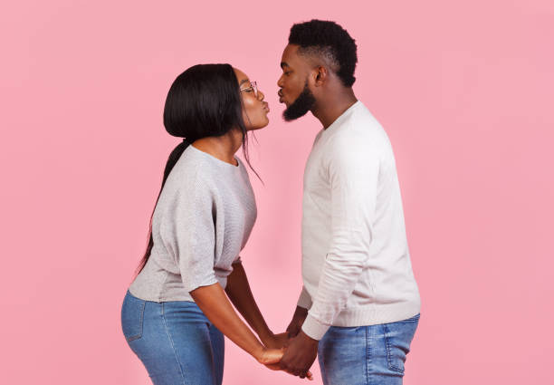 Couple standing together holding hands and kissing each others Side view of affectionate african couple standing together, holding hands and kissing each others against pink studio background cute couple stock pictures, royalty-free photos & images