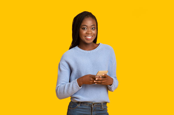istock Smiling young black woman using smartphone on yellow background 1189335574