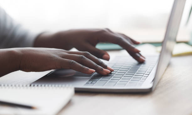 Black woman typing on laptop keyboard while working in office Closeup of unrecognizable afro woman typing on laptop keyboard while working in office, panorama keypad photos stock pictures, royalty-free photos & images