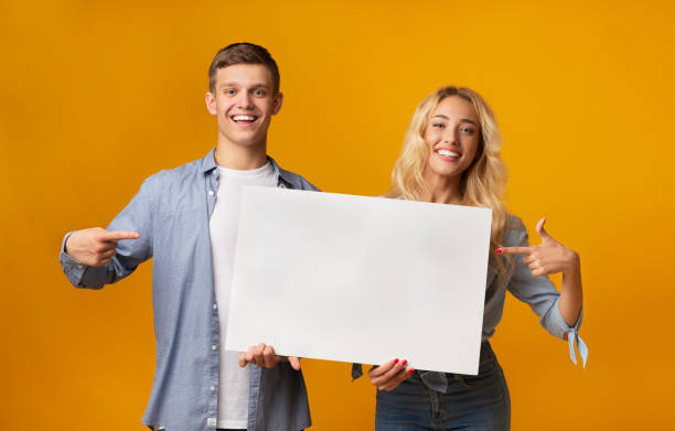 istock Young couple holding blank advertising board and pointing on it 1189337065