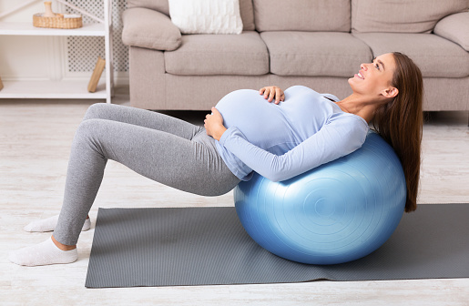Pregnant Woman Working Out With Fitness Ball At Home, Doing Exercises, Preparing For Childbirth