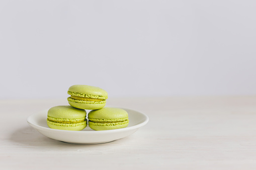 Three light green french macarons on a white plate and wooden table. Pistachio macarons. Place for text. Close-up.