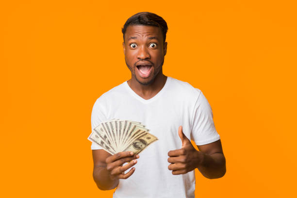 istock Surprised Black Man Holding Money Gesturing Thumbs-Up Standing, Studio Shot 1189339390