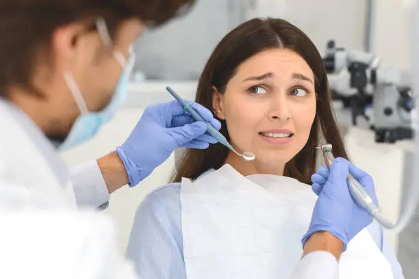 Dentophobia concept. Scared young woman looking at dentist