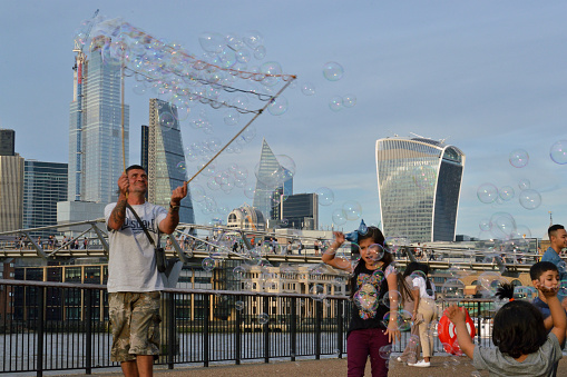 London/UK, August 24, 2019 - Man making giant soap bubbles on Thames river bank with St Paul's Cathedral in background