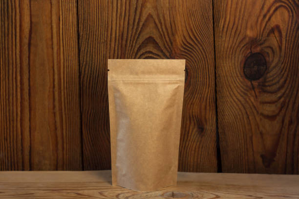 braune kraft papierbeutel taschen mit kaffeebohnen frontansicht auf einem holzhintergrund. verpackungen für lebensmittel und waren. - paper rough kraft foods brown stock-fotos und bilder