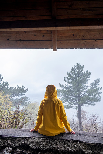 Person in Yellow Rain Coat sitting in a Shelter in Mountains Back View