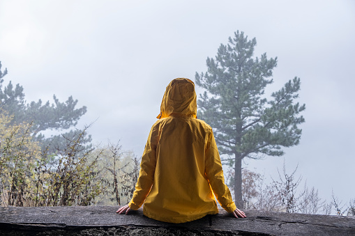 Person in Yellow Rain Coat sitting and looking at view Back View