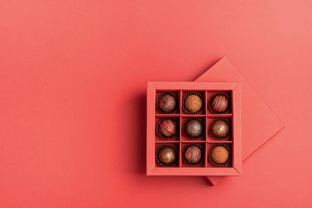 schokoladenbonbons in einer roten handwerksbox auf einem hellen korallenhintergrund. flaches layout . urlaubskonzept - chocolate candy stock-fotos und bilder