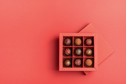 Chocolate candies in a red craft box on a bright coral background. Flat layout . Holiday Concept