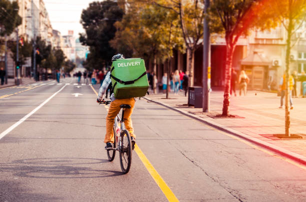 City Food delivery by bike Delivery man food service courier on bicycle in town. Rear view of man riding a bicycle in the city street with green bag on back biker photos stock pictures, royalty-free photos & images