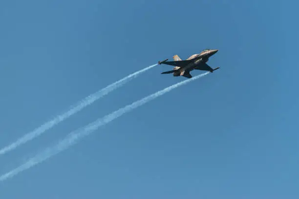 F-16 fighting military fighter jet airplane flying with smoke against blue sky background.