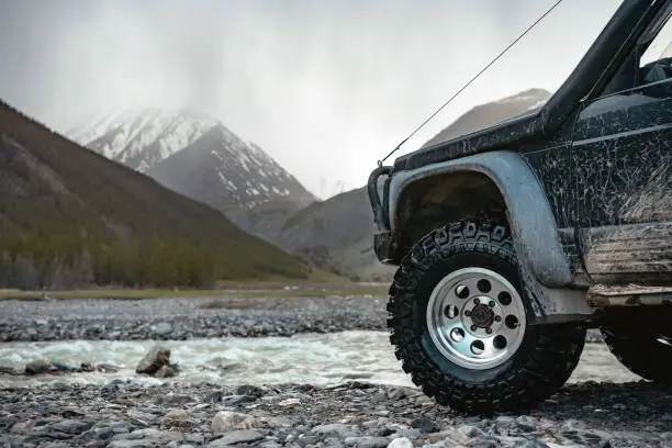 Big extreme offroad ready car wheel against mountains and river