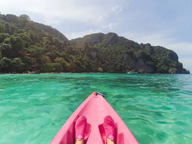 Photo of View from a pink kayak to the nose of a kayak and a green island in the clear water of the ocean.