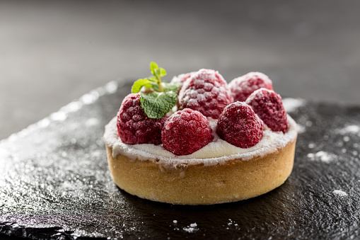 Raspberry tartlets with icing sugar close up on stone board on black background