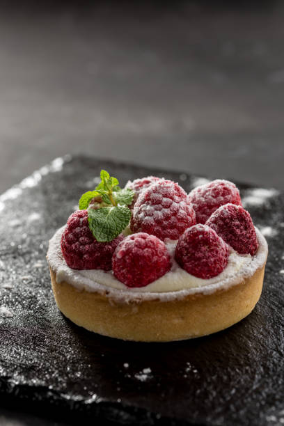 istock Raspberry tartlets with icing sugar close up on stone board on black background 1189360784