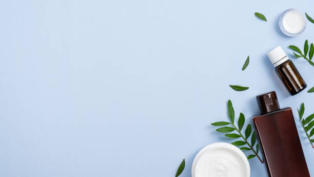 istock Flat lay composition with organic cosmetic products on blue background with copy space. Top view essential oil, lotion, cream jar and green leaves. Natural organic beauty product concept. 1189362304