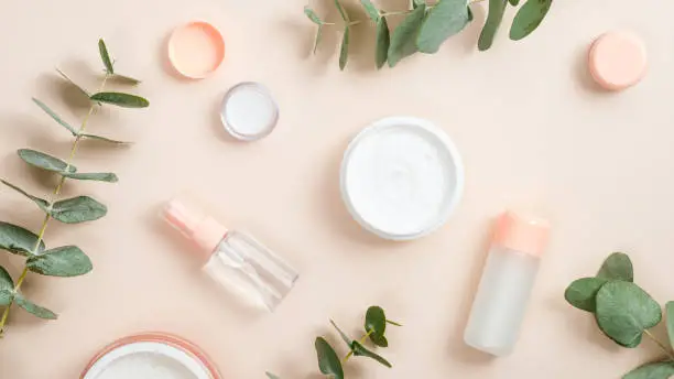 Photo of Flat lay composition with natural organic cosmetic products on beige background. Top view hand cream in jar, essential oil, skin lotion and eucalyptus leaves. Natural organic beauty product concept