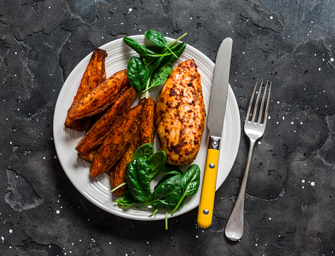 Baked chicken breast with sweet potatoes and spinach on a dark background, top view. Balanced healthy lunch