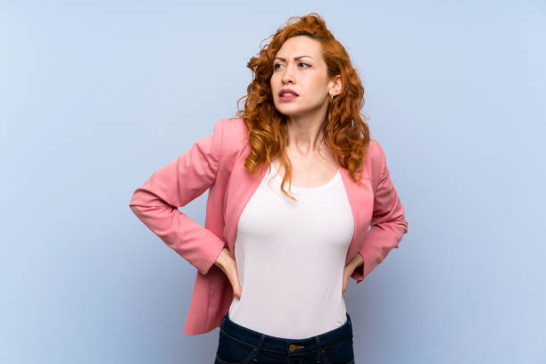 istock Redhead woman in suit over isolated blue wall suffering from backache for having made an effort 1189366239