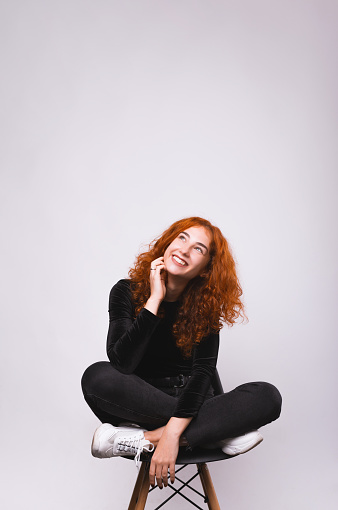 Happy smiling curly ginger girl, sitting on char in lotus position and looking up