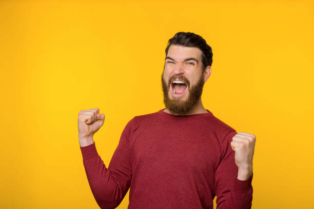 istock Bearded guy screaming and celebrating his triumph with rised hands, over yellow background 1189368341