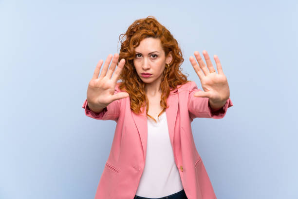 istock Redhead woman in suit over isolated blue wall making stop gesture and disappointed 1189371010