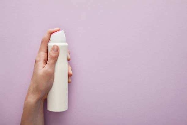 opinião cortada da mulher que prende o desodorante do pulverizador no fundo violeta com rosas brancas - deodorizing - fotografias e filmes do acervo