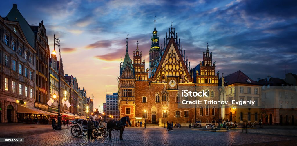 Wroclaw central market square with old houses, Town Hall and sunset, horse and carriage. Wroclaw central market square with old houses, Town Hall and sunset, horse and carriage. Panoramic night view, long exposure.  Historical capital of Silesia, Wroclaw (Breslau) , Poland, Europe. Wroclaw Stock Photo
