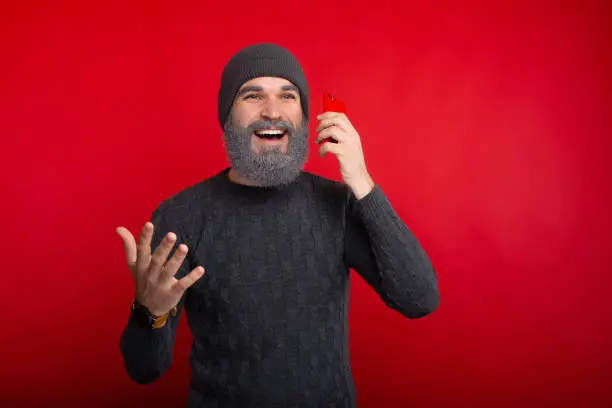 Handsome man with white beard talking on smartphone near red background